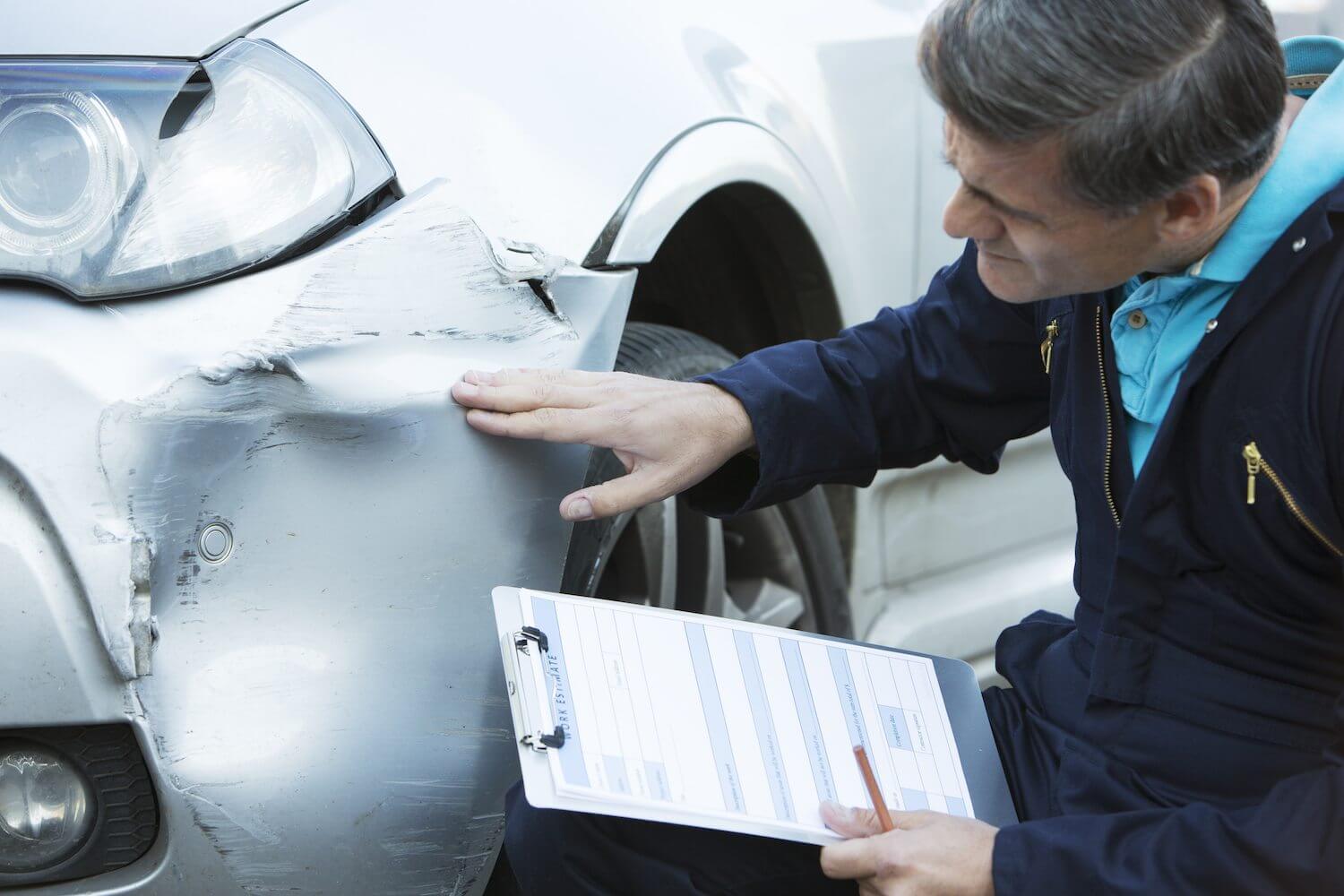 Auto body technician inspects a damaged car fender and bumper, preparing an estimate for vehicle collision repair.
