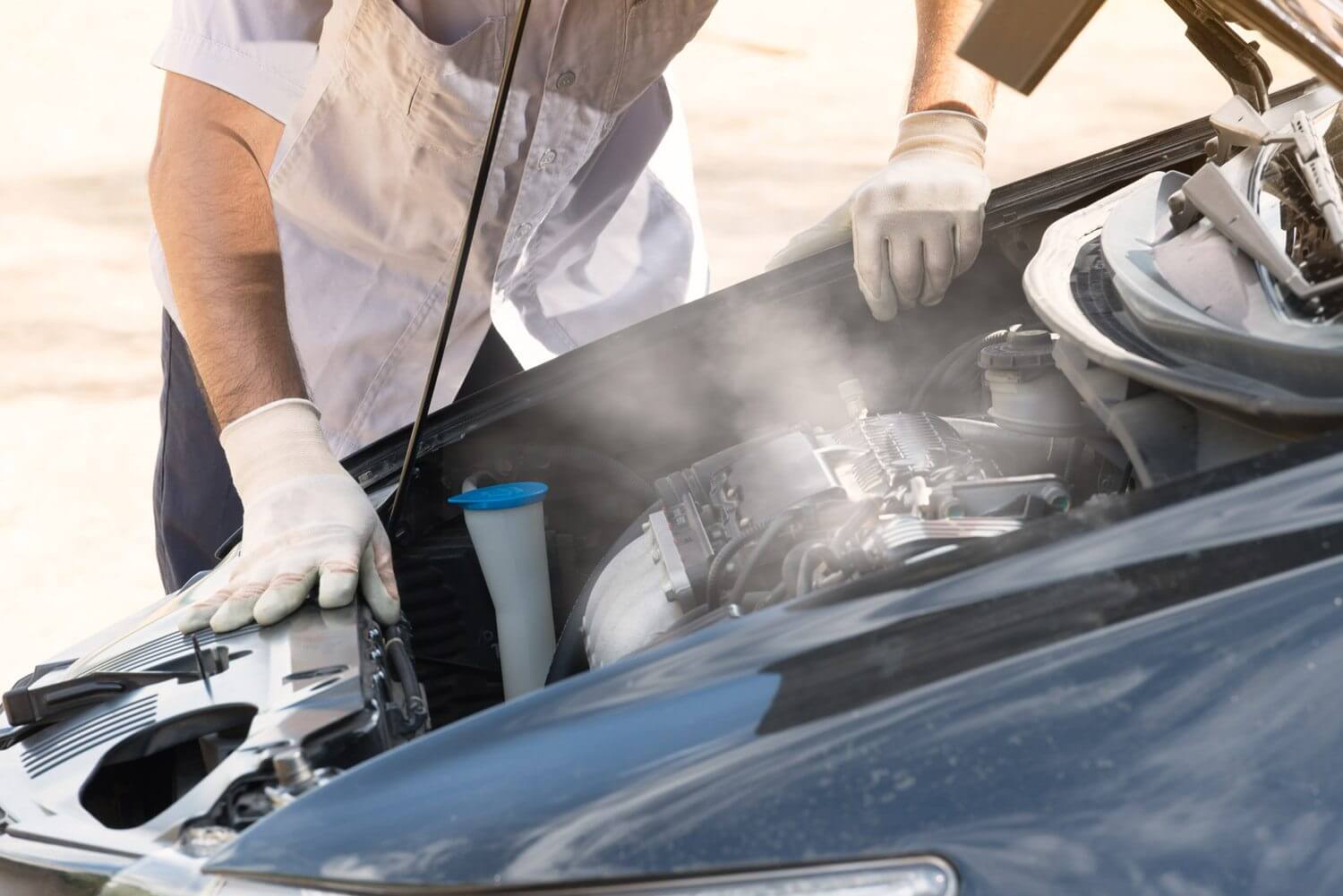Person in gloves inspects a steaming car engine with the hood open, needing domestic and imported vehicle repair services.